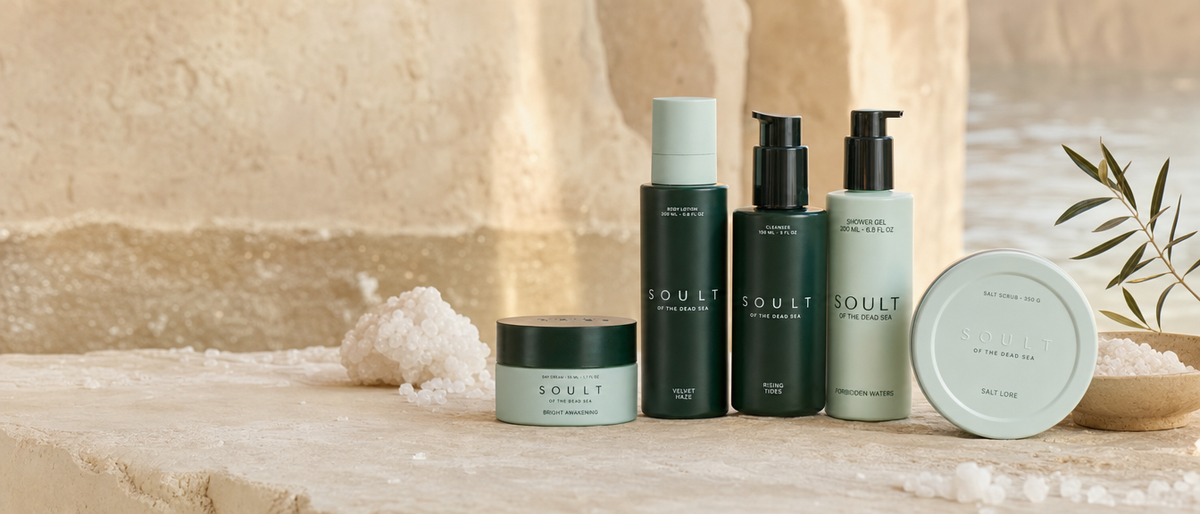 Soult of the Dead Sea skincare: body lotion, facial cleanser, shower gel, day cream and salt scrub on a sunlit limestone ledge with Dead Sea salt crystals