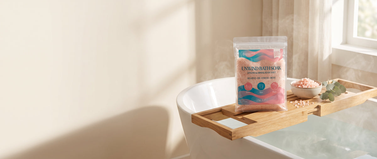 Essentially Young Unwind Bath Soak, Epsom and Himalayan salt, on a bath caddy beside a bowl of pink salt